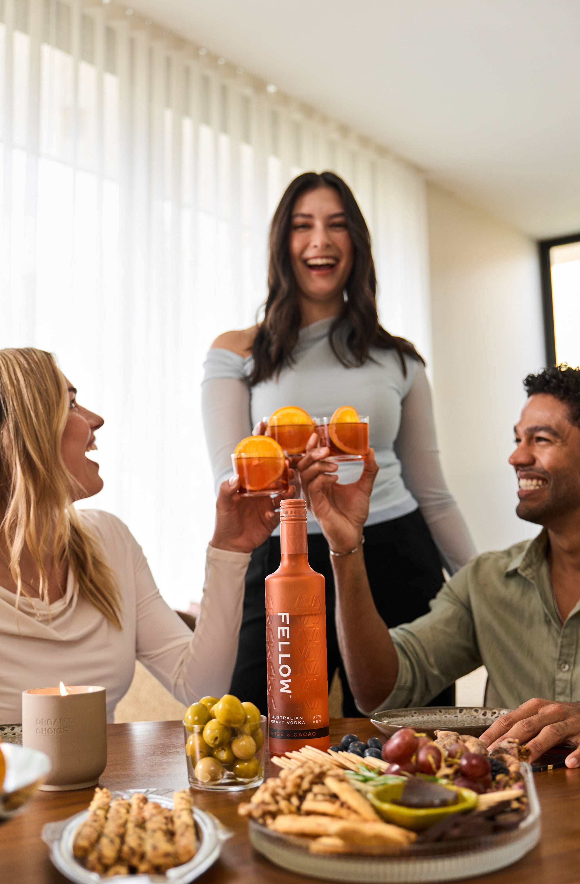 Three people at a table with food and drinks, including a bottle labeled 'Fellow'.
